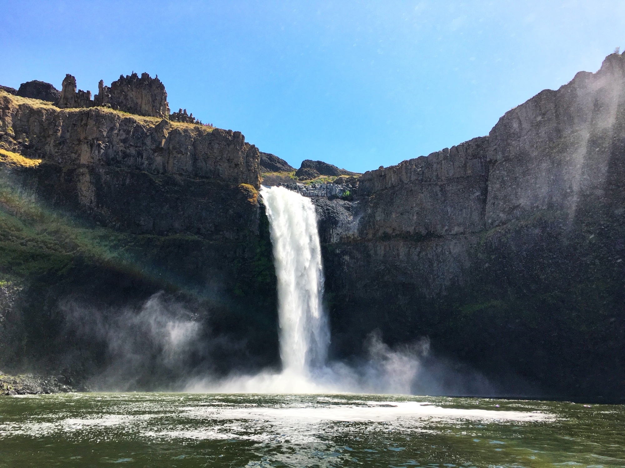 Palouse Falls roaring into a dark basalt canyon from below, mist rising in the sunlight