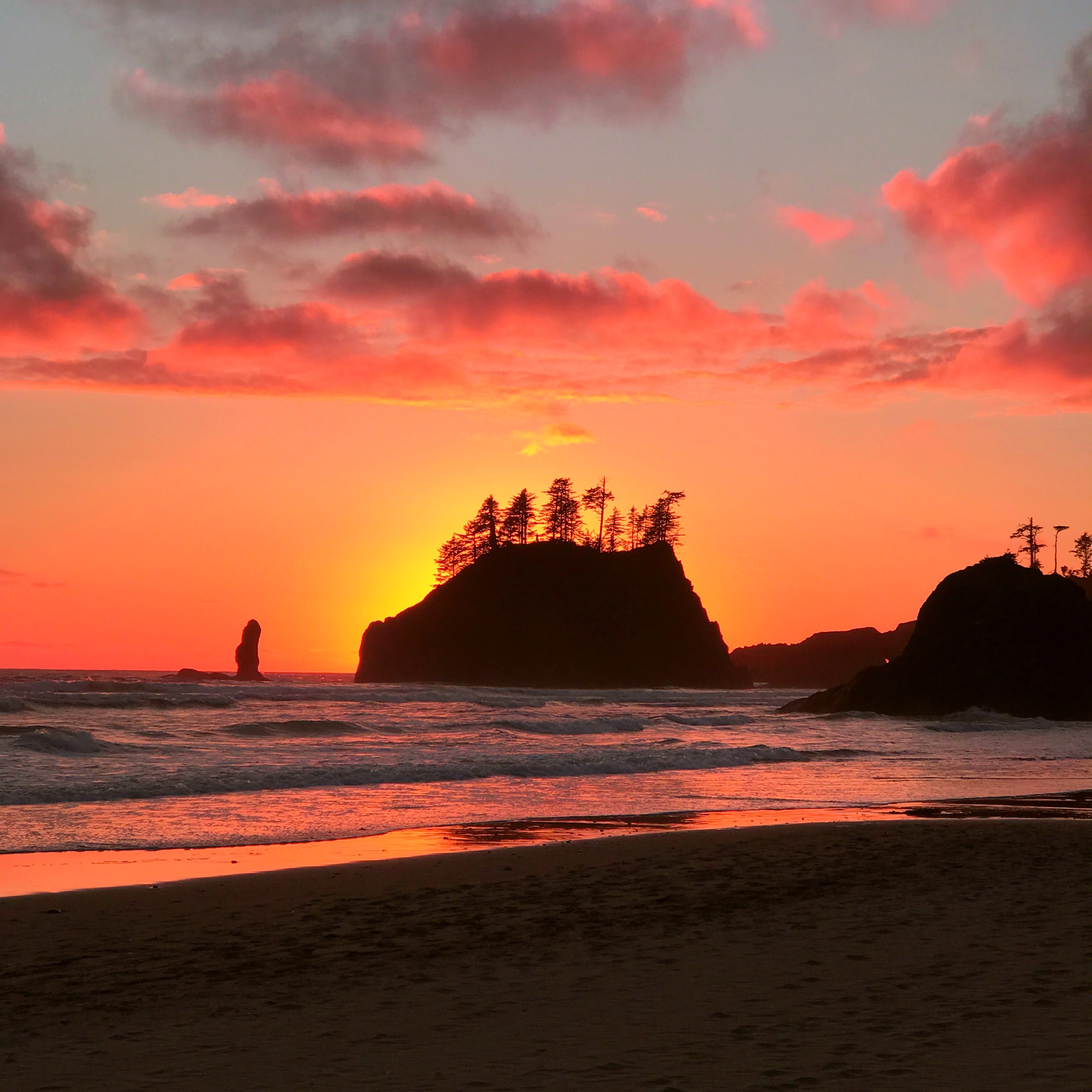 Blazing orange and red sunset silhouetting sea stacks on a Pacific coast beach, waves rolling in