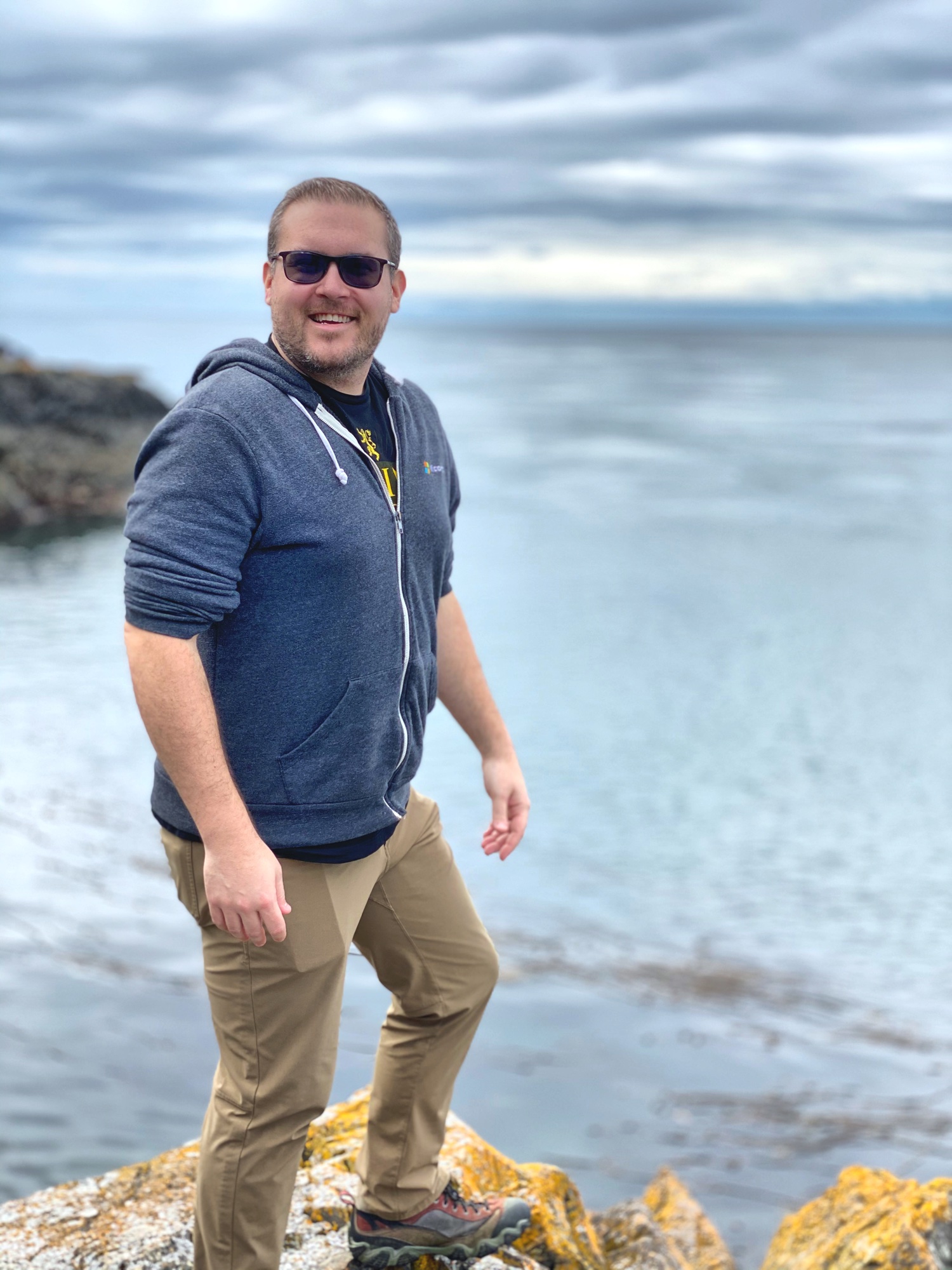 Jon smiling on a rocky coastline with the ocean stretching behind him
