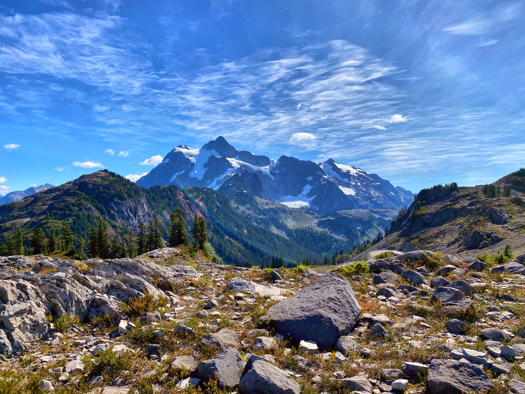 Mount Shuksan rising above a rocky alpine meadow under a vivid blue sky with wispy clouds