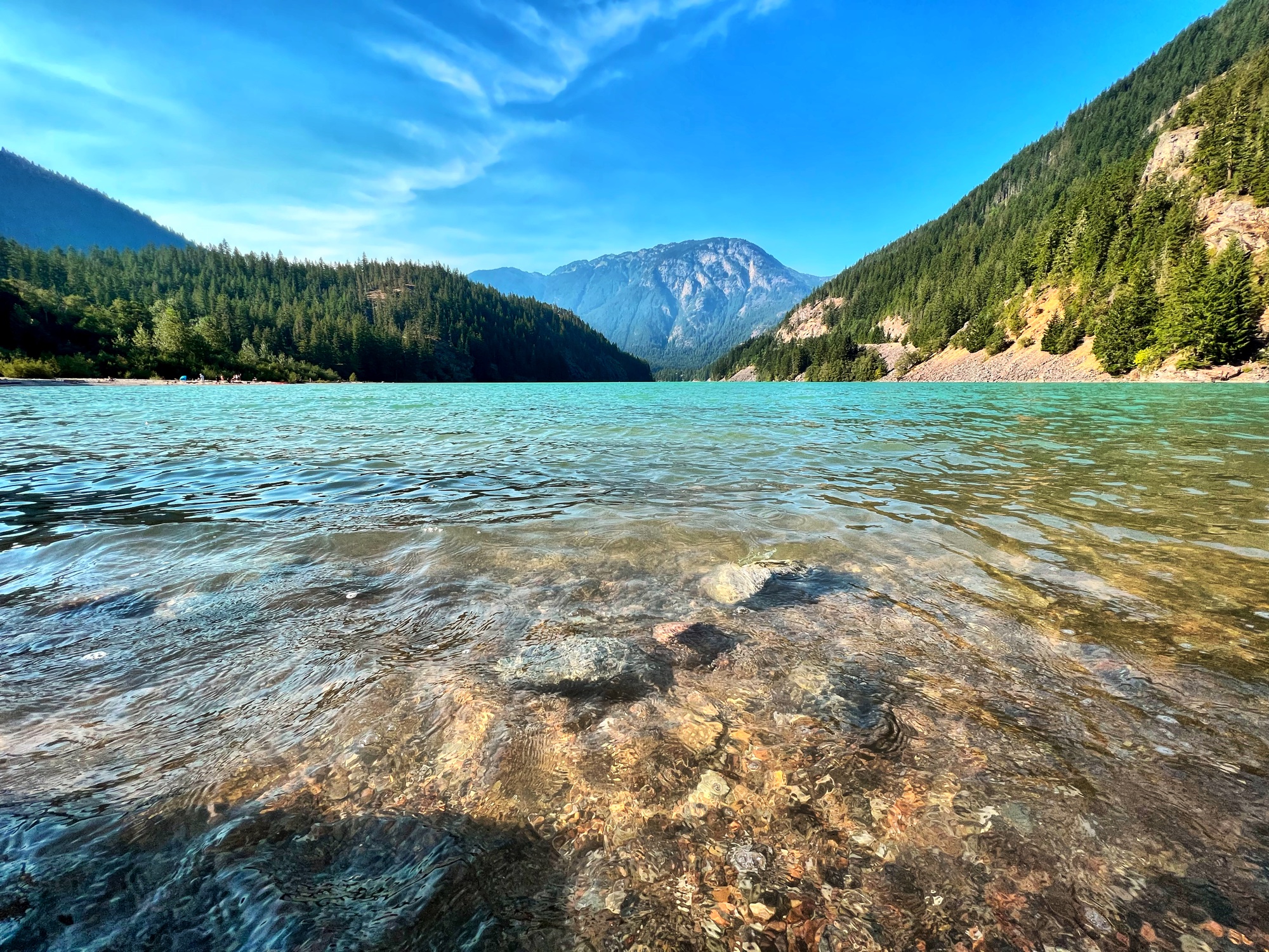 Crystal clear turquoise glacial lake with mountains and forest reflected in the water