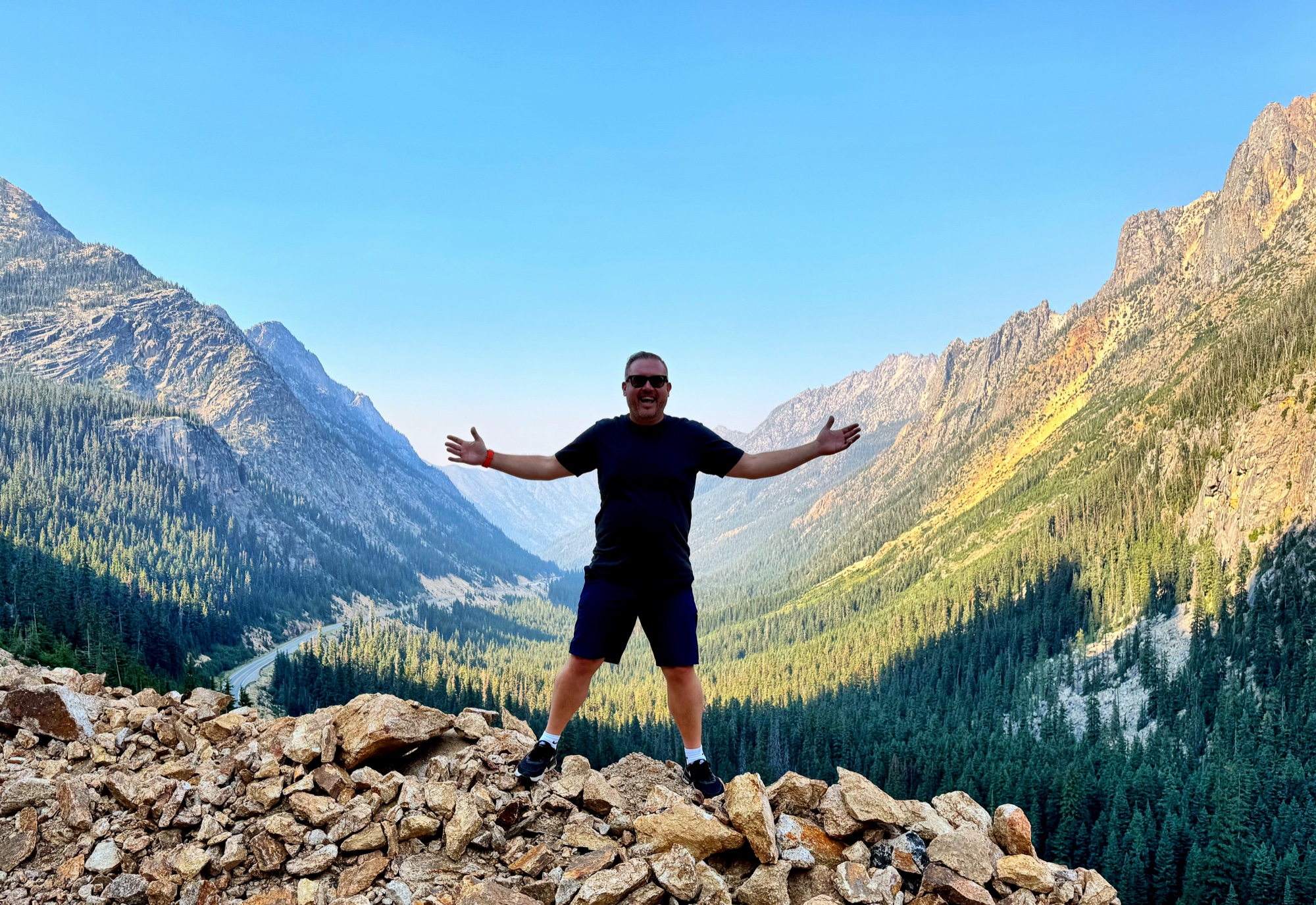Jon with arms wide open on a mountain summit