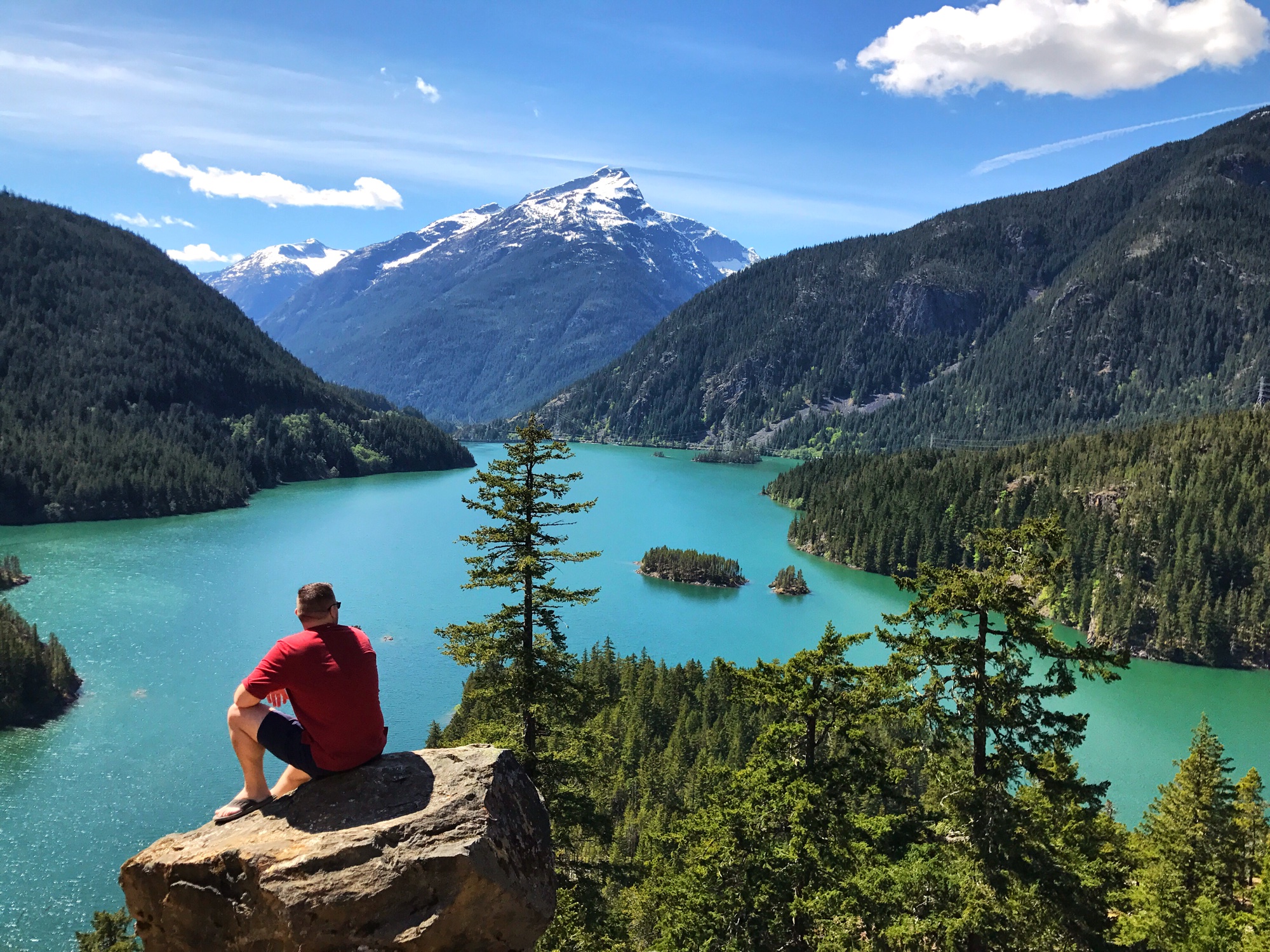 Jon sitting on a cliff overlooking the stunning turquoise waters of Diablo Lake with mountains behind