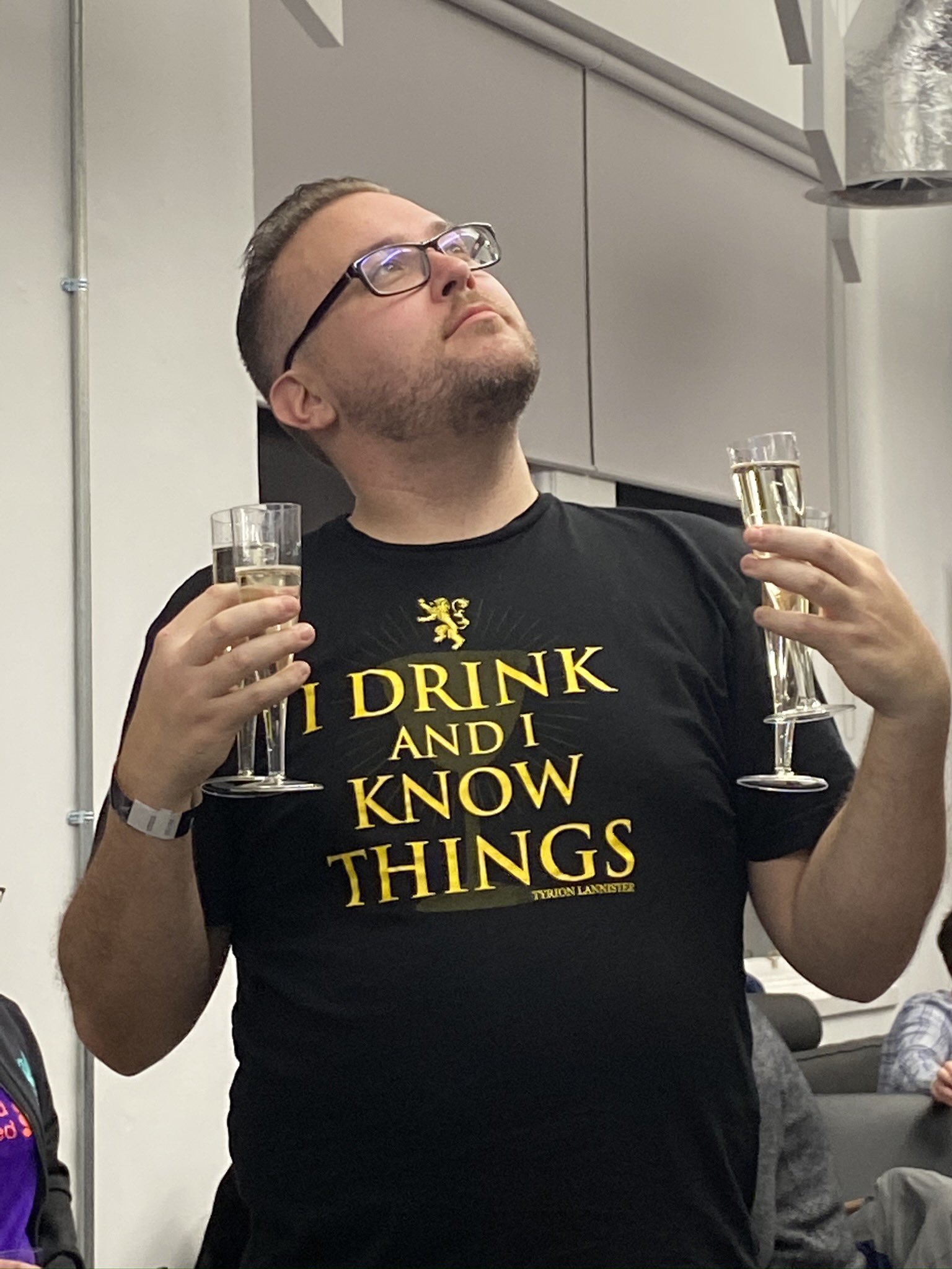 Jon wearing an I Drink and I Know Things shirt, holding two champagne flutes with a regal expression