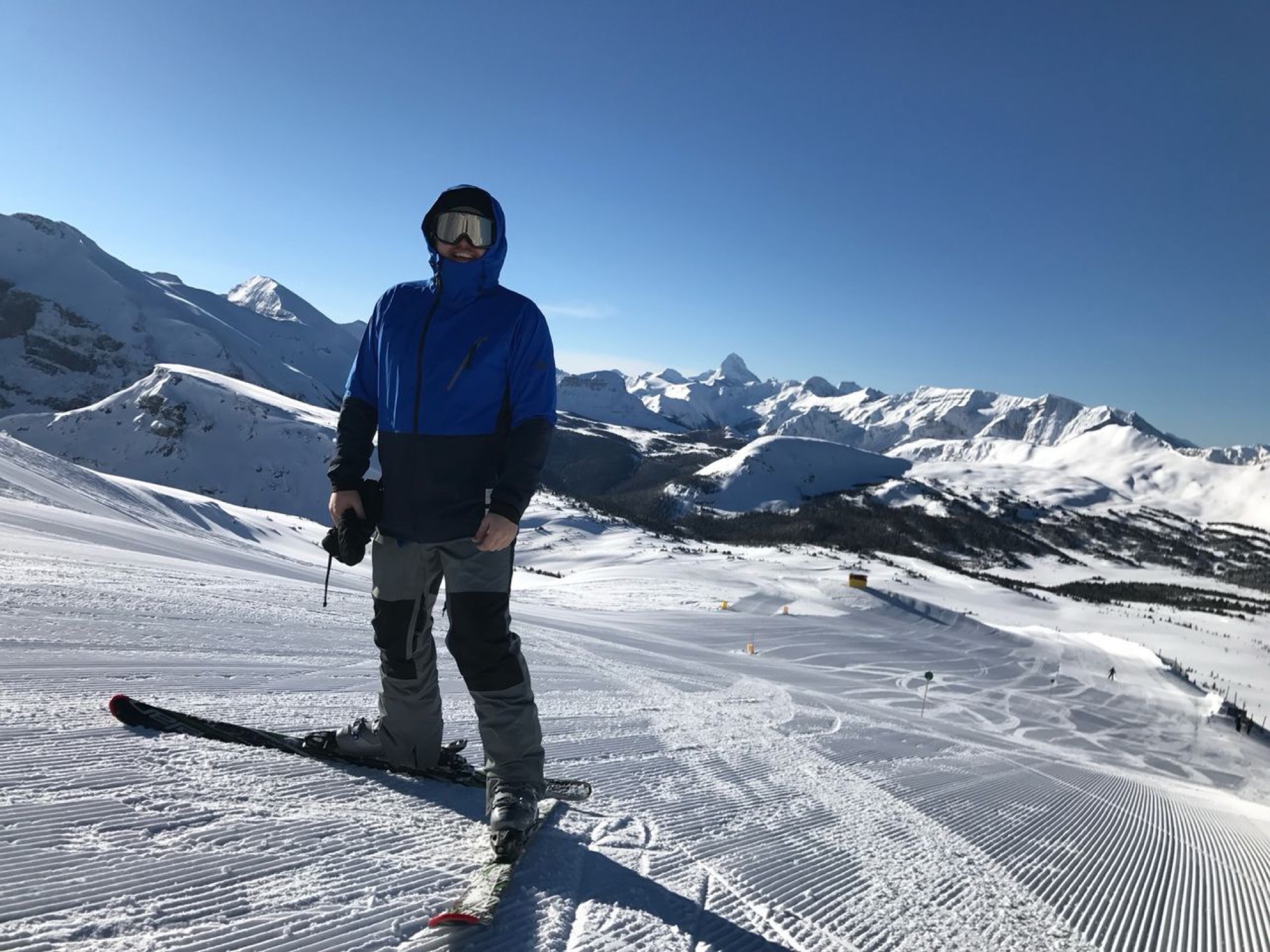 Jon standing on skis on a bluebird day with a vast snow-covered mountain range stretching behind him