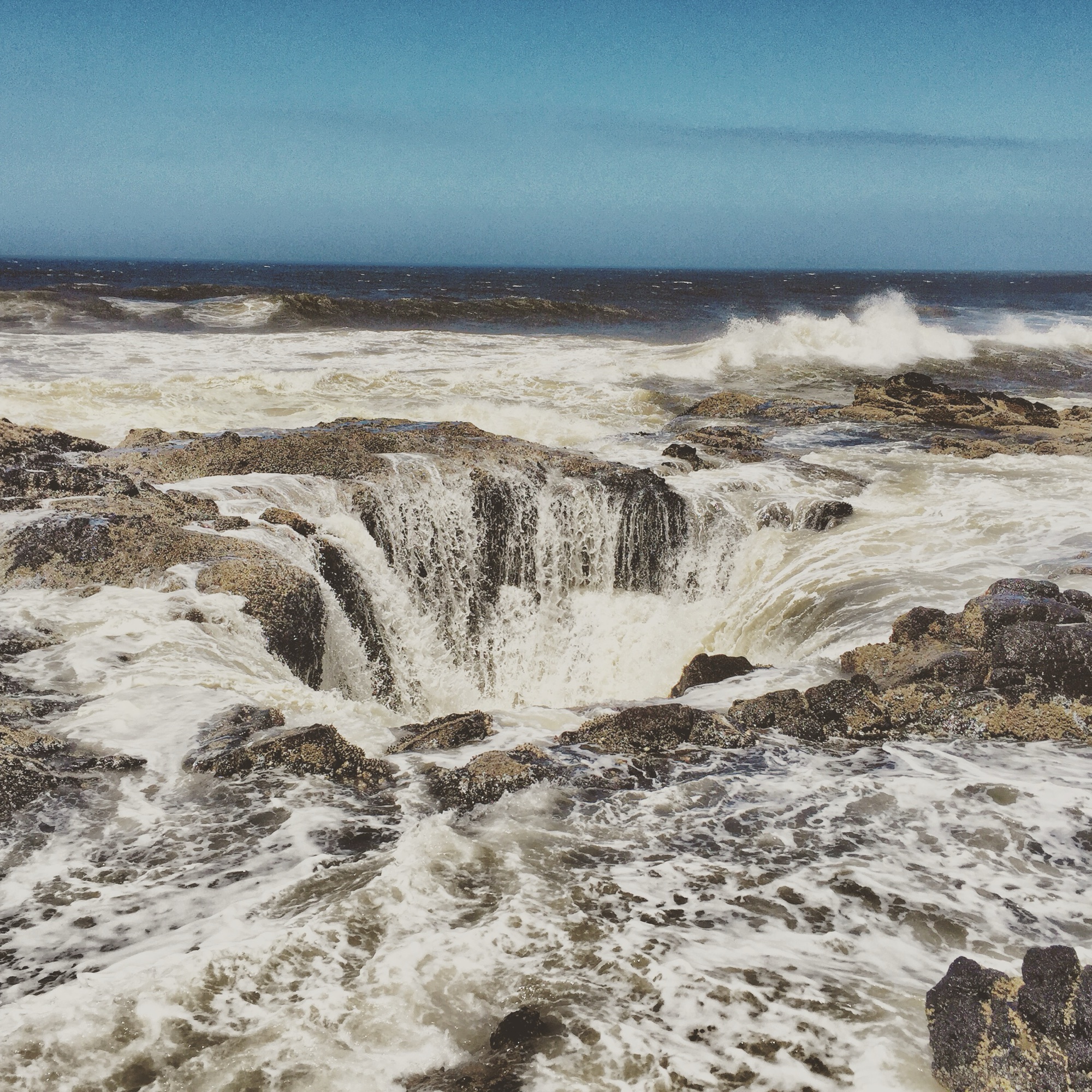 Thor's Well on the Oregon coast — a natural sea drain in rocky shoreline with waves crashing in and pouring down