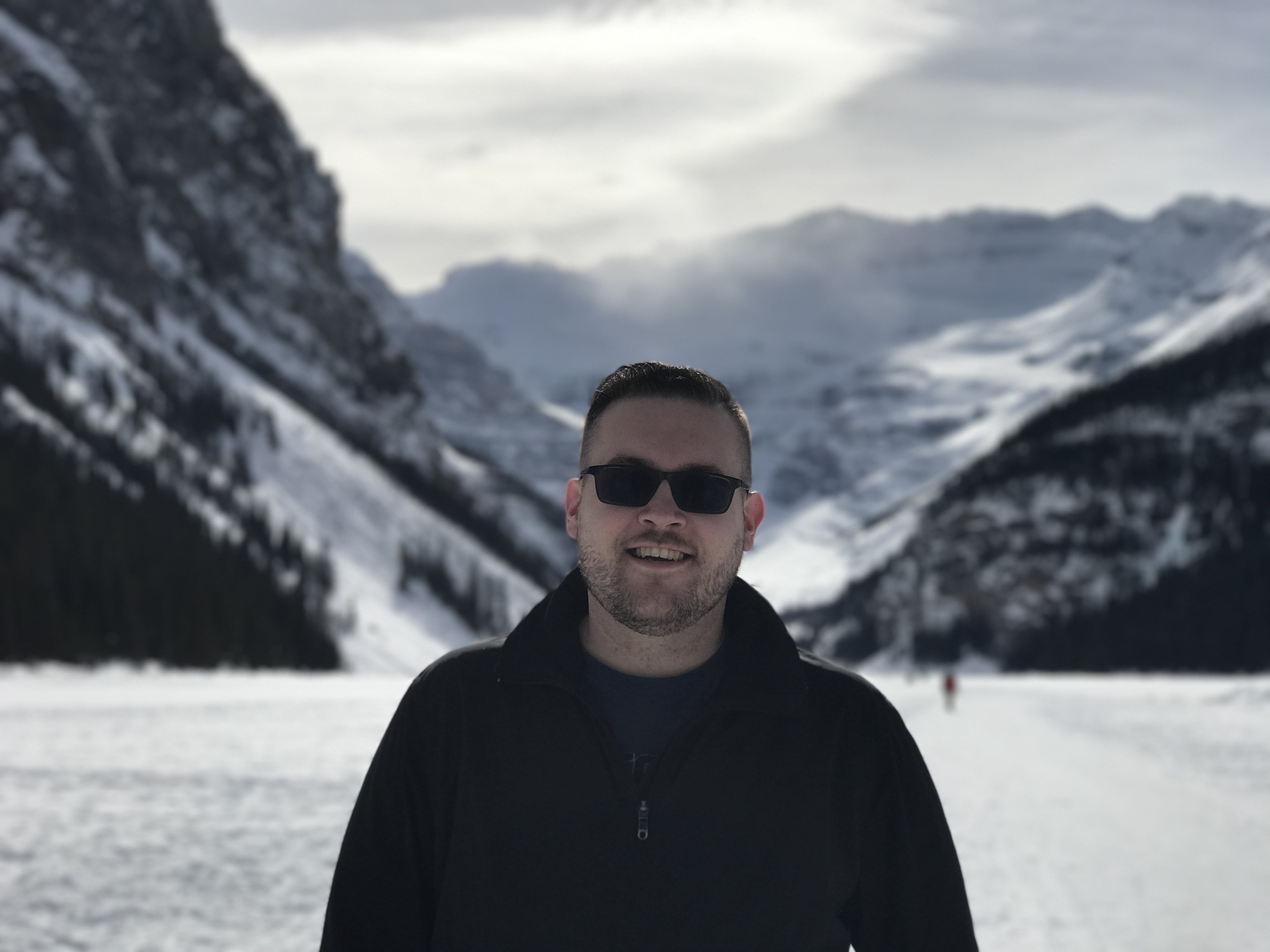 Jon smiling in front of frozen Lake Louise with dramatic snowy mountains behind
