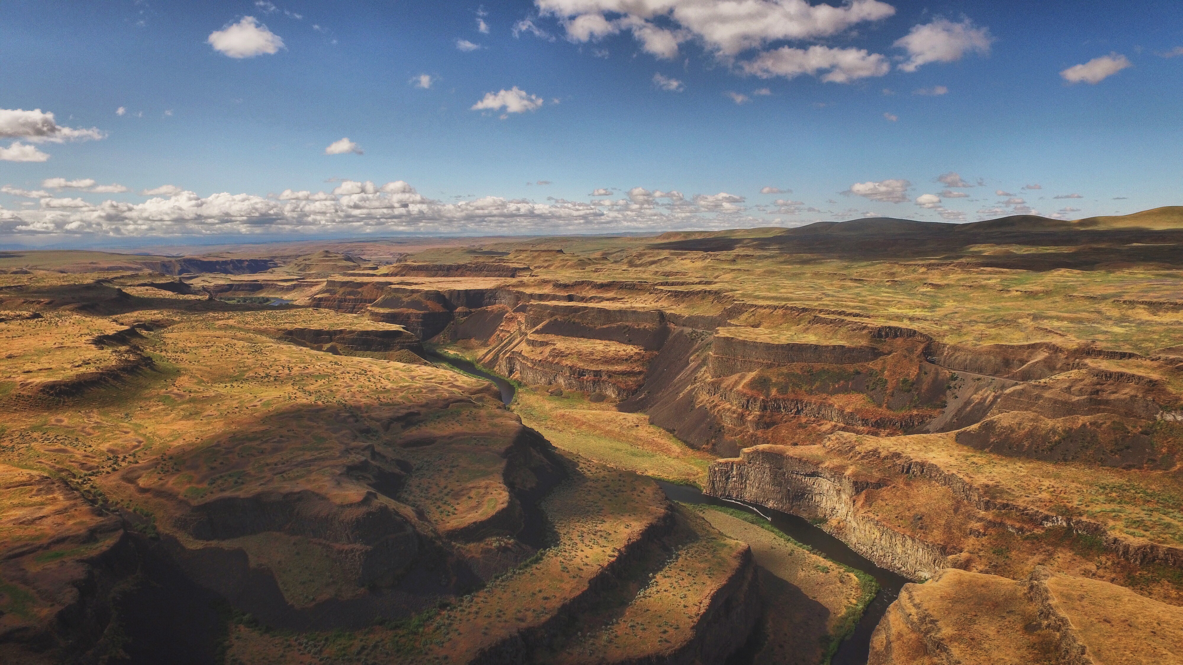 Aerial view of a dramatic canyon with layered basalt walls and a river snaking through the bottom under a partly cloudy sky