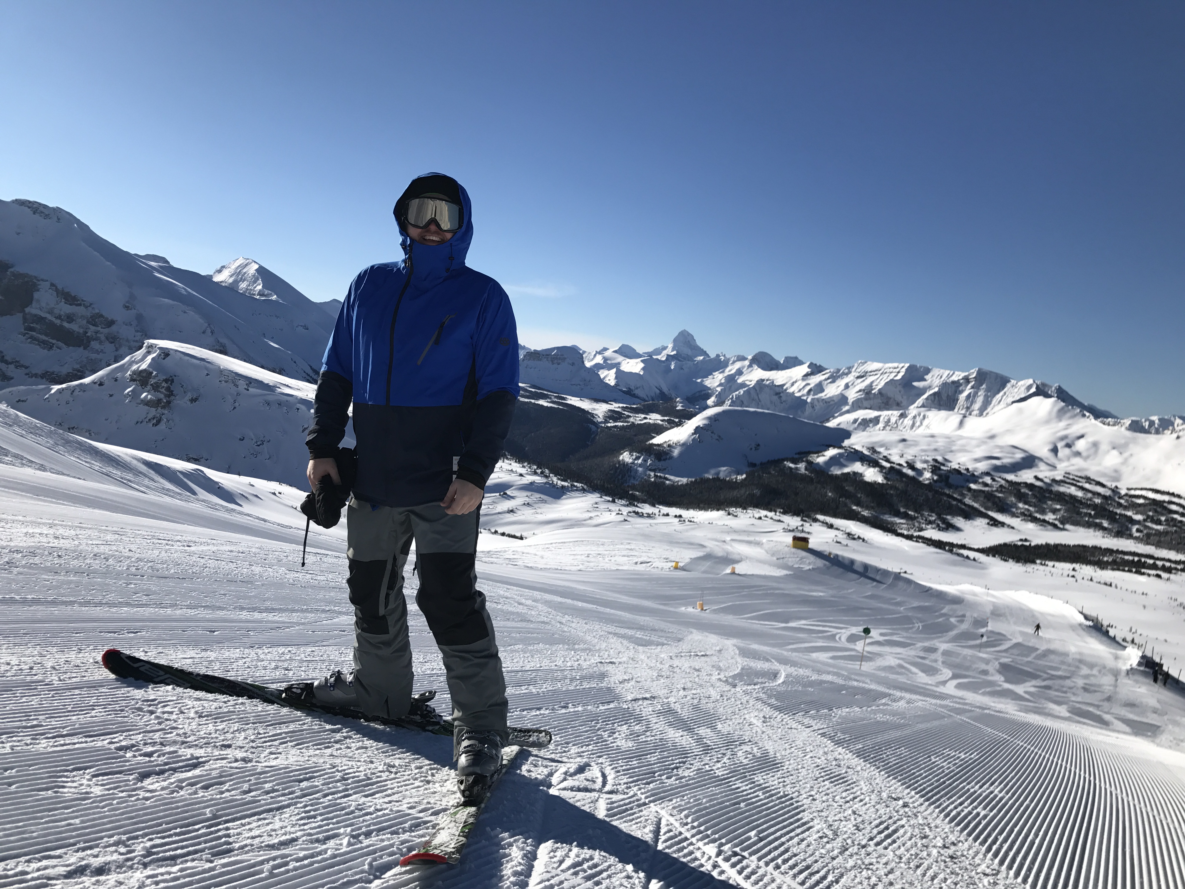 Jon on skis on a bluebird day with dramatic mountain peaks in the background
