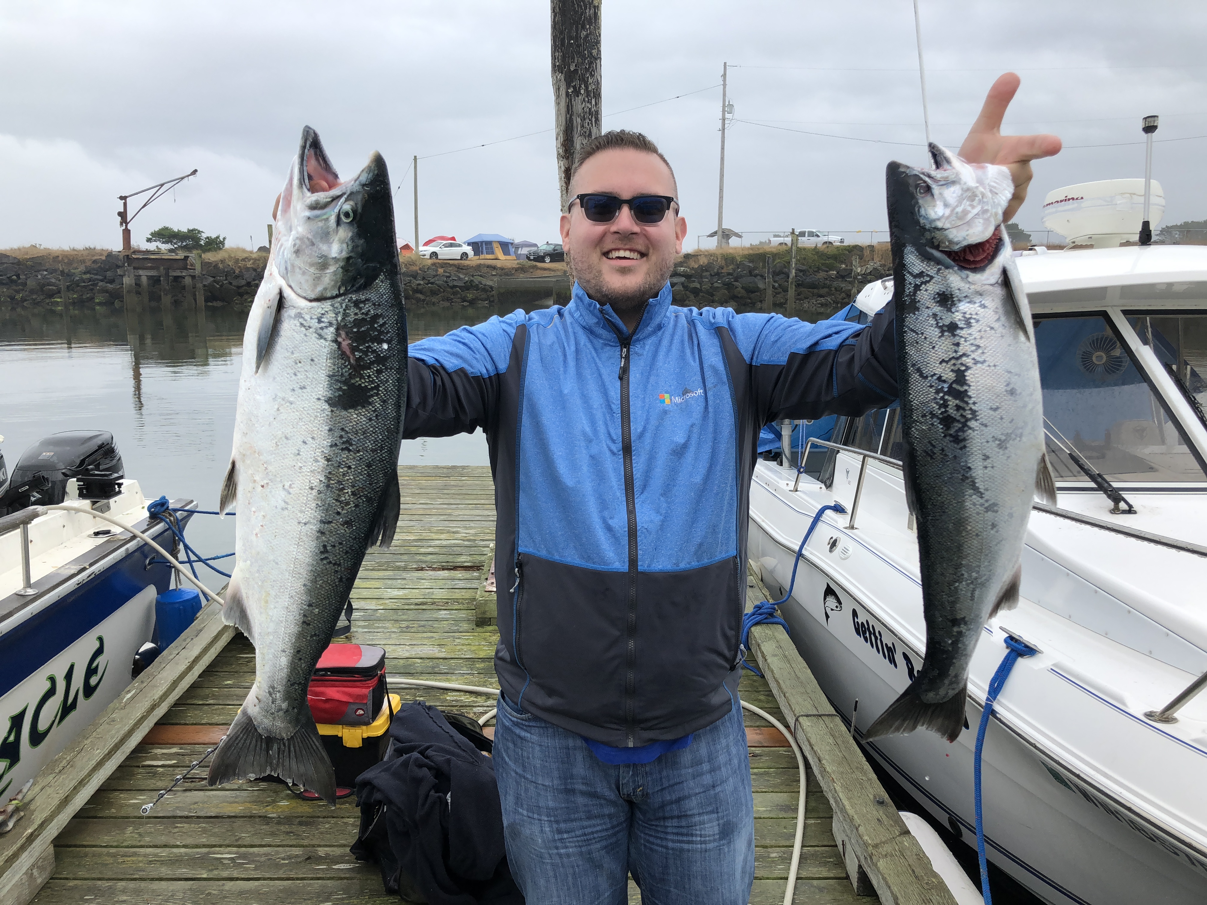 Jon holding two enormous salmon with a massive grin on a fishing dock