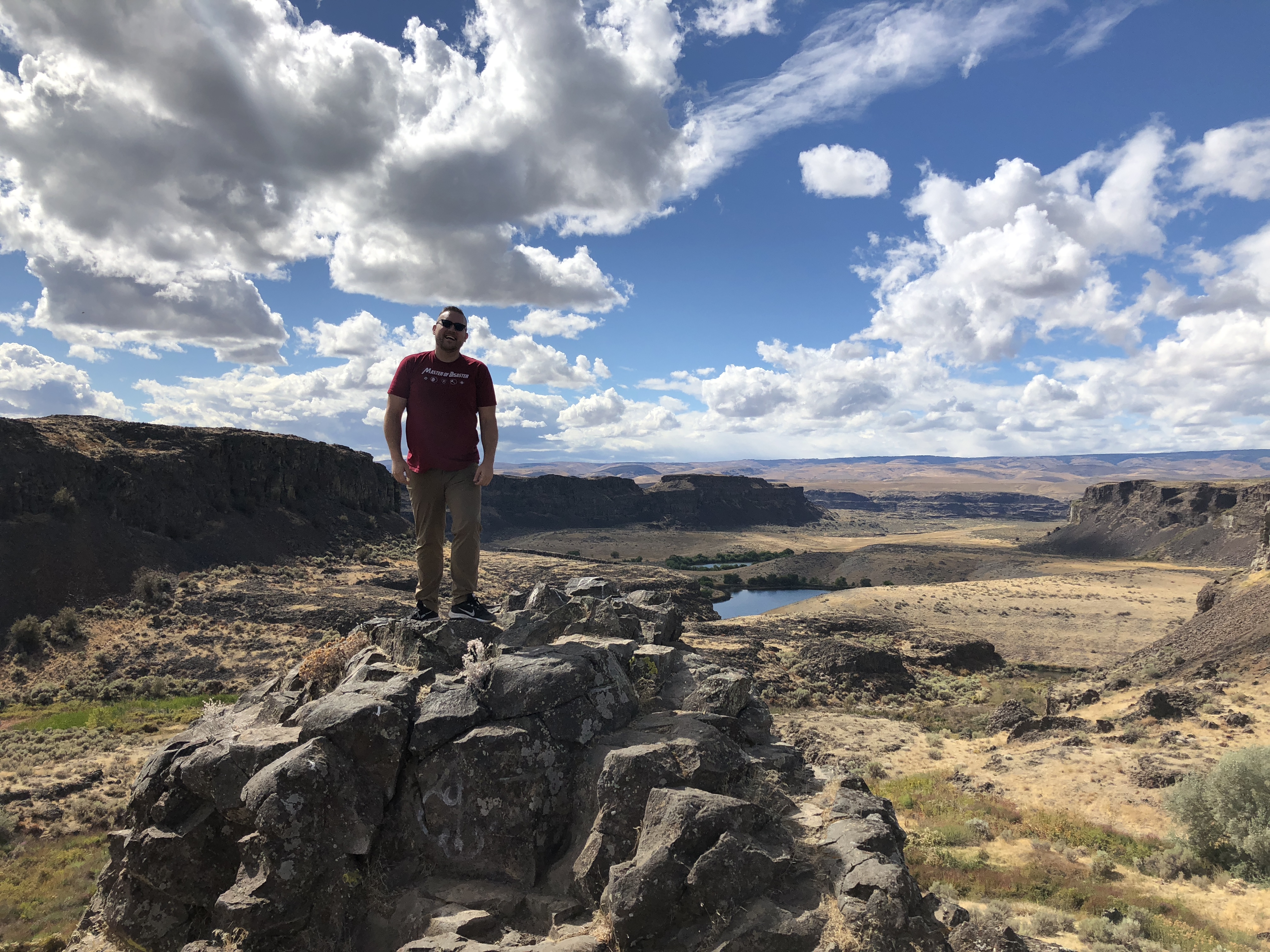 Jon standing on a rocky basalt formation with a sweeping desert canyon landscape behind