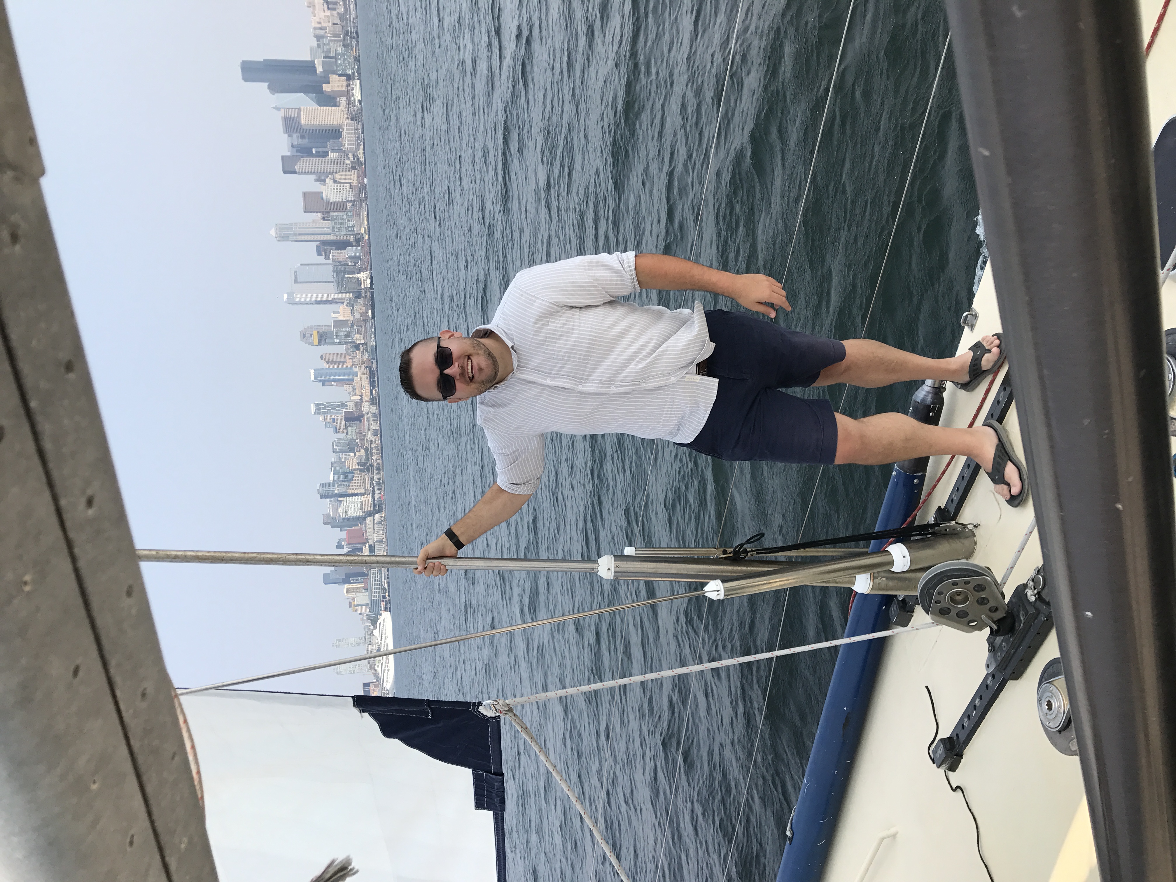 Jon smiling on the deck of a sailboat with the Seattle skyline stretching across the water behind him
