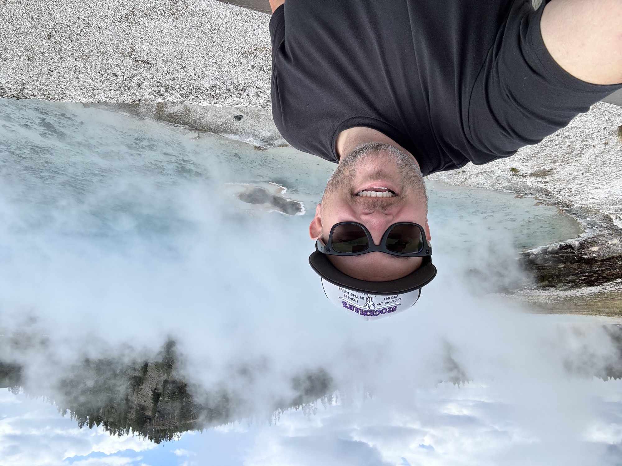 Jon selfie in front of a steaming turquoise hot spring pool, thermal mist rising into the sky behind him